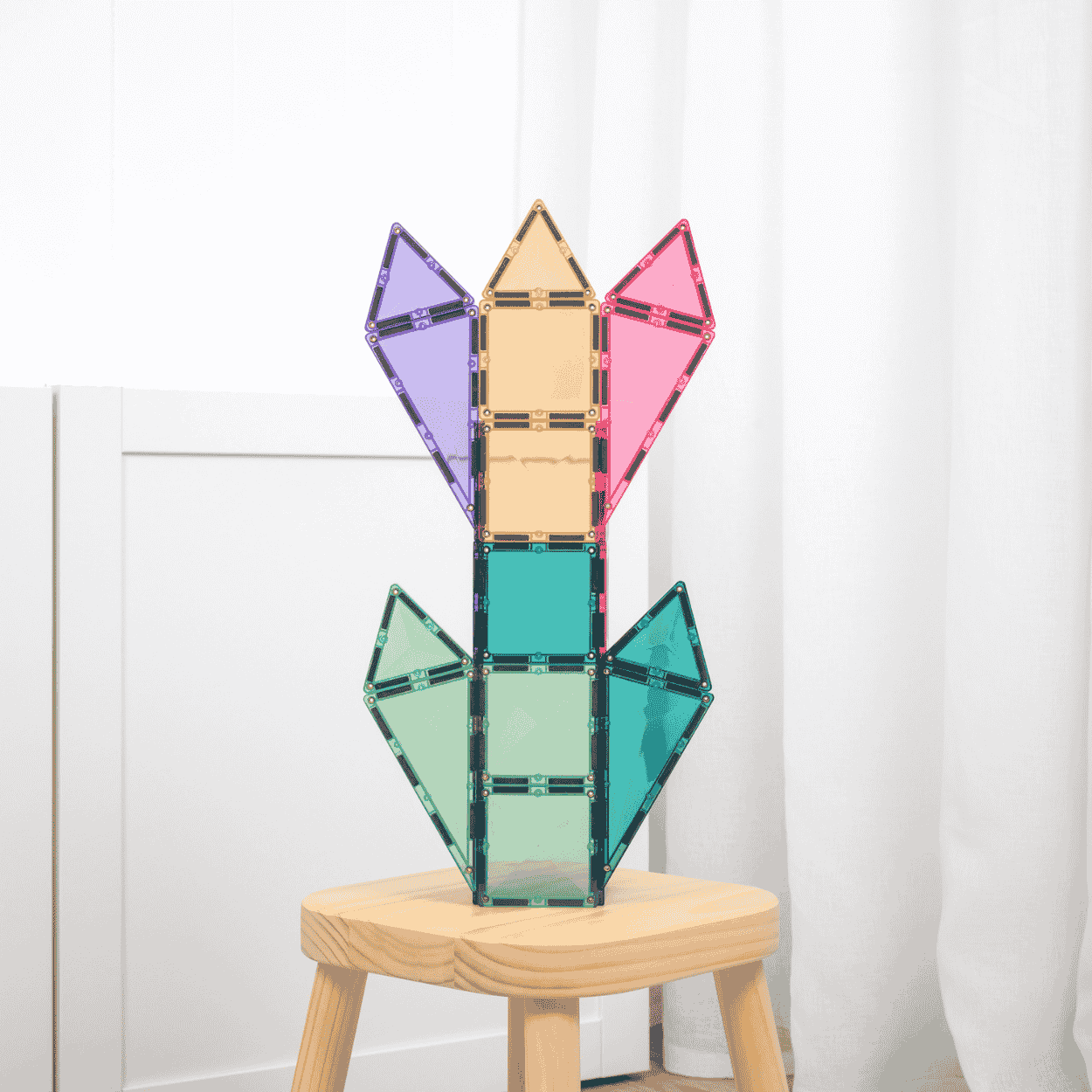 Colorful magnetic tiles plant structure on a wooden stool against a white curtain background